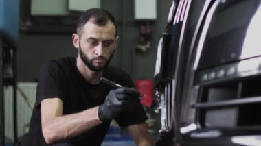 Siyah eldivenli bir adam arabanın ön ızgarasını fırçalar. Bir oto yıkama işçisinin yakın plan fotoğrafı.