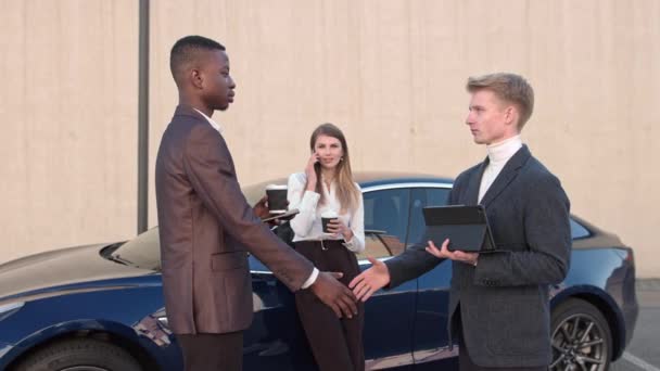 Dos hombres de negocios saludan cerca de la oficina en el fondo de un coche deportivo cerca del cual se encuentra una joven chica de negocios hablando por teléfono. Un hombre afroamericano da la mano a un joven como señal de — Vídeos de Stock