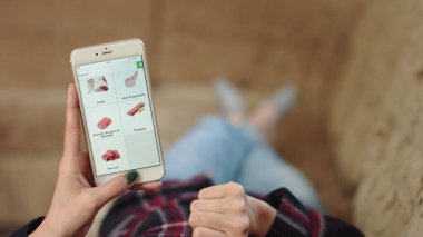 Evdeki Kadın Oturma Odasında Kanepede Uzanıyor İnternet 'ten Akıllı Telefon Alıyor. Çevrimiçi bir mağazada akıllı telefon kullanarak et siparişi veren kadın. Kadın Market Çevrimiçi Mağazasında Et Seçiyor. POV