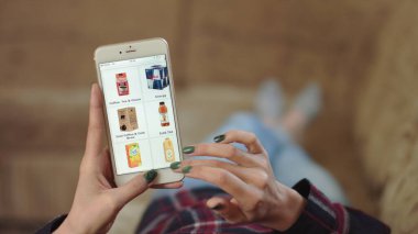 Evdeki Kadın Oturma Odasında Kanepede Uzanıyor İnternet 'ten Akıllı Telefon Alıyor. Kadın akıllı telefon kullanarak çevrimiçi bir mağazada içki sipariş ediyor. Kadın Market Çevrimiçi Dükkanından İçecek Seçiyor