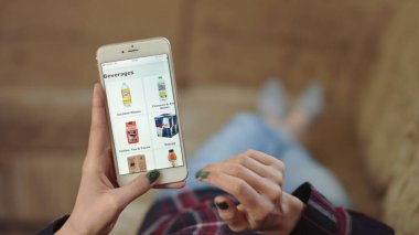 Evdeki Kadın Oturma Odasında Kanepede Uzanıyor İnternet 'ten Akıllı Telefon Alıyor. Kadın akıllı telefon kullanarak çevrimiçi bir mağazada içki sipariş ediyor. Kadın Market Çevrimiçi Dükkanından İçecek Seçiyor