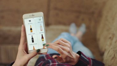 Evdeki Kadın Oturma Odasında Kanepede Uzanıyor İnternet 'ten Akıllı Telefon Alıyor. Kadın, Smartphone kullanarak çevrimiçi bir mağazada şarap sipariş ediyor. Kadın Market İnternetindeki Şarapları Seçiyor. POV