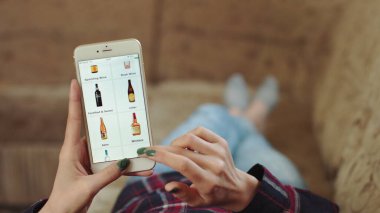 Evdeki Kadın Oturma Odasında Kanepede Uzanıyor İnternet 'ten Akıllı Telefon Alıyor. Kadın, Smartphone kullanarak çevrimiçi bir mağazada şarap sipariş ediyor. Kadın Market İnternetindeki Şarapları Seçiyor. POV