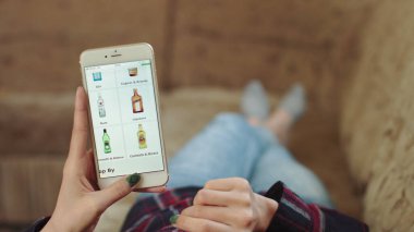 Evdeki Kadın Oturma Odasında Kanepede Uzanıyor İnternet 'ten Akıllı Telefon Alıyor. Kadın, Smartphone kullanarak çevrimiçi bir mağazada şarap sipariş ediyor. Kadın Market İnternetindeki Şarapları Seçiyor. POV