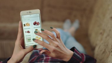 Evdeki Kadın Oturma Odasında Kanepede Uzanıyor İnternet 'ten Akıllı Telefon Alıyor. Çevrimiçi bir dükkanda akıllı telefon kullanarak peynir siparişi veren bir kadın. Kadın Bakkalda Çevrimiçi Peynir Seçiyor