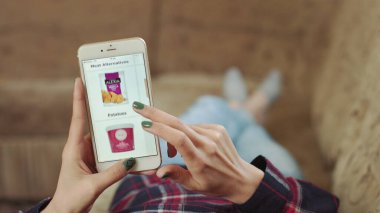 Evdeki Kadın Oturma Odasında Kanepede Uzanıyor İnternet 'ten Akıllı Telefon Alıyor. Çevrimiçi bir dükkanda akıllı telefon kullanarak dondurma siparişi veriyor. Kadın Market Çevrimiçi Dükkanından Dondurma Seçiyor.