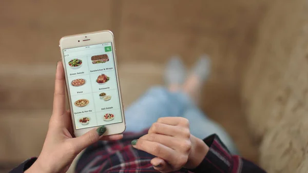 Femme à la maison Allongé sur le canapé dans le salon en utilisant Smartphone achète dans Internet Shop. Femme commande des aliments préparés à la maison dans une boutique en ligne à l'aide d'un smartphone. La femelle choisit des aliments préparés à l'épicerie Photo De Stock