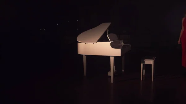 Ein junges schönes Mädchen in einem roten Kleid nähert sich dem weißen Klavier und setzt sich. Verbindung von klassischer Musik. Romantisches Ambiente Saal voller Rauch — Stockfoto