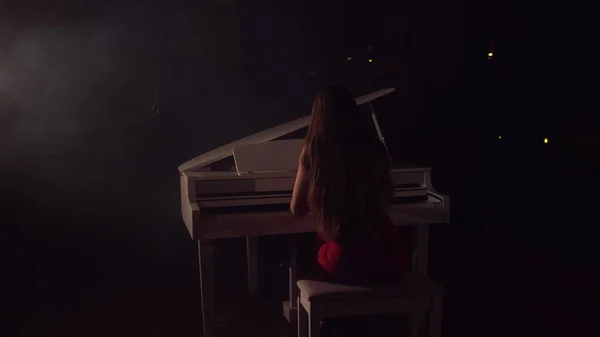 4K Footage Of Female Pianist Plays In Beautiful Grand Piano On Stage In Concert . A woman plays the piano in the concert hall. Stage light and light fog on the background