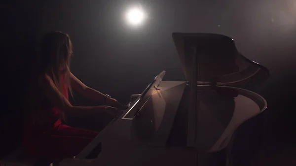 4K Footage Of Female Pianist Joue Dans Le Beau Piano à Grand Piano Sur Scène En Concert. Une femme joue du piano dans la salle de concert. Lumière de scène et brouillard lumineux sur le fond Image En Vente