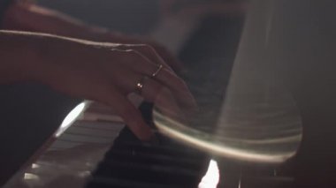 Kadın piyanist, güzel bir kuyruklu piyanoda yavaş çekimde hafif klasik müzik çalar. Piyano tuşları koyu renklerde kapanır. Ön planda ışıktan ve dumandan parlıyor