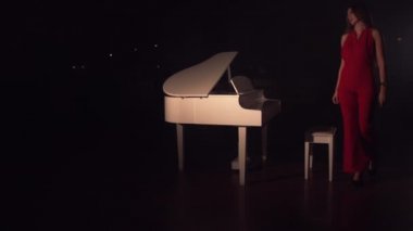 Kırmızı elbiseli genç güzel bir kız beyaz piyanoya yaklaştı ve oturdu. Klasik müzik konsepti. Romantik atmosfer salonu dumanla dolu