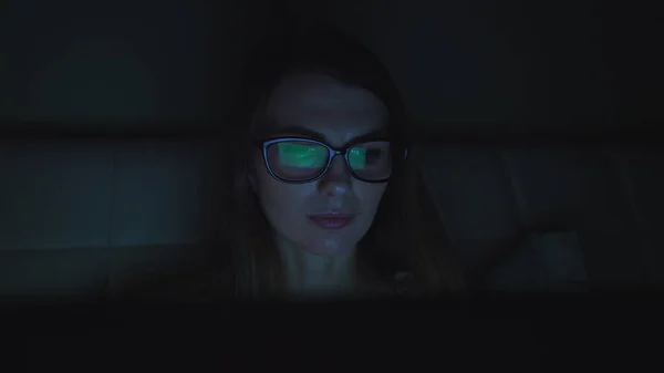 Portrét mladé dívky v brýlích, dívky ležící na pohovce s laptopem a psacím vzkazem. Noc. Polštář pod hlavou jedné dívky. V obýváku není světlo. Obrazovka světla na dívčí tvář — Stock fotografie