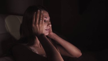 Genç kız bir dizüstü bilgisayarla kanepede uzanıyor ve birkaç kez esniyor. Geceleri çalışmaya çalışıyorum. Uzun saçlı ve beyaz gömlekli bir kız. Bacakları ekoseyle kaplı.