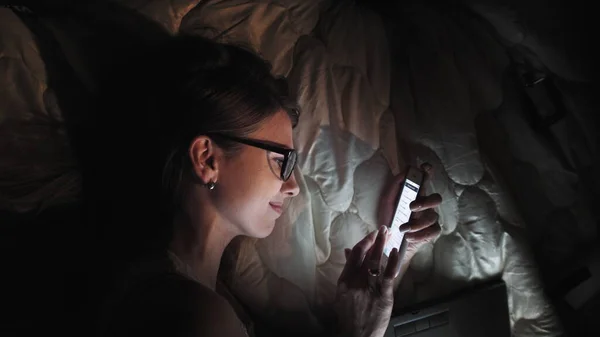 Menina adolescente na tela sensível ao toque Laptop inteligente e fones de ouvido na cama, estudante em quarto escuro com luz noturna móvel, uma jovem mulher estudando e lendo à noite. — Fotografia de Stock