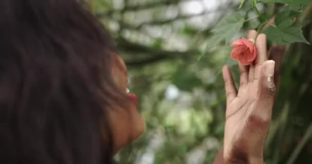 Young beautiful African American woman with natural makeup in the rainforest, botanical garden. Close-up shot of a flower and then the focus shifts to the girls eyes. Cut girl in summer dress — 图库视频影像