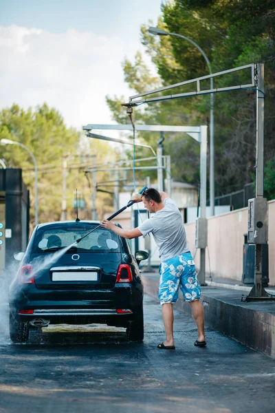 Summer Car wash. Man holding a high-pressure water sprayer washing the car headlight.Contactless self-service car wash. Cleaning the car with high pressure water