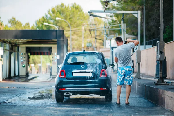 Bilvask, nærbilde av en mann som holder en vannspray under høyt trykk og vasker bilen med hodetelefoner. Rengjøring av stolen med vann under høyt trykk stockbilde