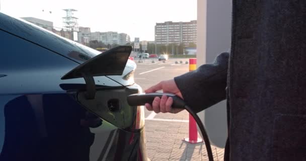 Een schot onder het luik waar de elektrische eco auto oplaadt. Het laadluik voor elektrische auto 's wordt automatisch geopend. Een mannelijke hand plaatst een erectiele auto oplaadkabel. — Stockvideo