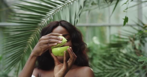 Porträtt av en ung vacker flicka av blandras med två halvor av ett äpple i händerna framför kameran och separera dem. Begreppet: hälsosam livsstil, naturlig kroppsvård vitaminer — Stockvideo