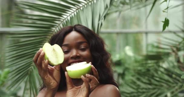 Portret van een jong mooi meisje van gemengd ras dat twee helften van een appel in haar handen houdt voor de camera en ze scheidt. Concept: Gezonde levensstijl, natuurlijke lichaamsverzorging vitaminen — Stockvideo