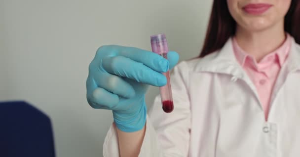 Γυναίκα γιατρός κάνει εξετάσεις αίματος στο εργαστήριο. Γιατρός ιολόγος σηκώνει το χέρι, δείχνει σωλήνα εξέταση αίματος. Εμβόλιο, θεραπεία ασθενειών. Πορτρέτο μιας όμορφης νεαρής γιατρού — Αρχείο Βίντεο