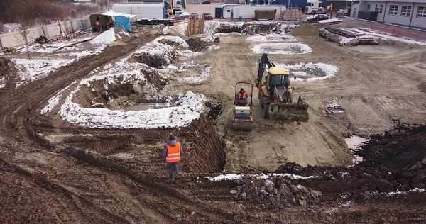 Veduta aerea di macchinari pesanti, trattore trasporto terra, preparazione costruzione. La pista di pattinaggio compatta il terreno. Inizio della costruzione del flick edificio. — Foto Stock