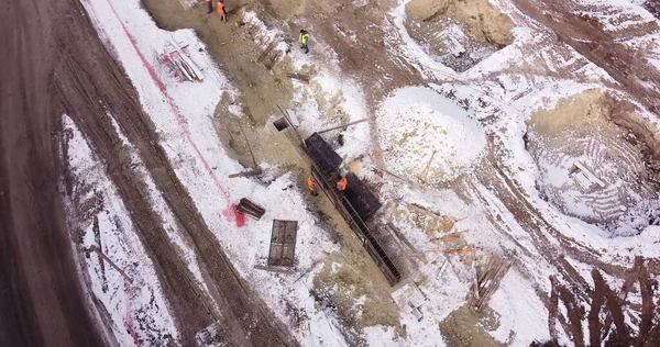 Los ingenieros trabajan con construcciones metálicas mientras construyen una casa. Vuelo aéreo sobre un sitio de desarrollo de nuevas construcciones. Vista de arriba hacia abajo en los contratistas en sombreros de seguridad. —  Fotos de Stock