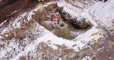 Bir evin inşaatında traktör. İnsansız hava aracı uçurmak, bir traktörün üzerinden uçmak. İşçi, temel betonun kalitesini kontrol eder. Bir endüstriyel tesisin inşaatı