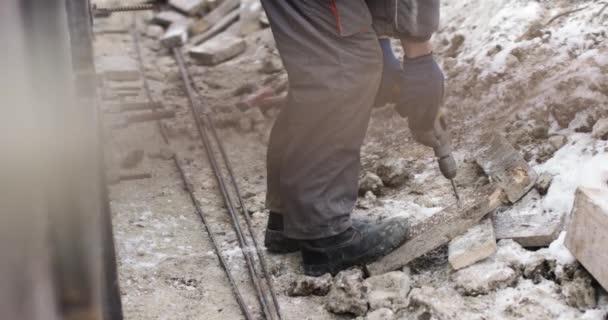 A construction company worker drills a hole in a wooden board. Work on the street in winter in difficult conditions — Stock Video