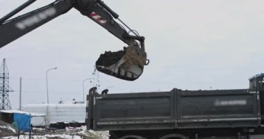 Kazıcı inşaat alanında faaliyet gösteriyor. Çekim: traktör kovası bir kamyonu dolduruyor. Bir kazıcı ve kamyon toprak yüklüyor. Endüstriyel bir tesisin inşasına hazırlanıyorum.