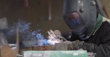 Koruyucu maskeli demirci metal ve demirle çalışıyor kaynak makinesi, parlak kıvılcımlar ve flaşlar kullanıyor.