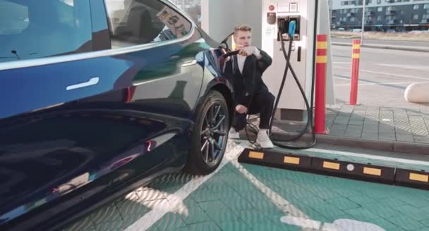 El hombre caucásico que carga el vehículo eléctrico del coche con la estación e-mobile de carga rápida de DC camina hacia y lejos tocando el adaptador de cable de carga — Vídeos de Stock