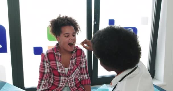 Médico afro-americano revisando paciente. A Girl Shows A Sore Throat To A Doctor By Opening Her Mouth. El pediatra vino a un paciente enfermo. Comprobación de la salud del niño. Admisión al hospital — Vídeos de Stock