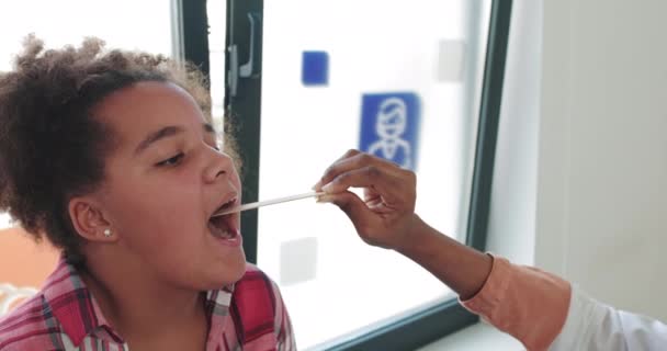 Una visita a un niño paciente por un médico de familia, pediatra. A Girl Shows A Sore Throat To A Doctor By Opening Her Mouth. Comprobación de la salud del niño. Admisión al hospital — Vídeo de stock