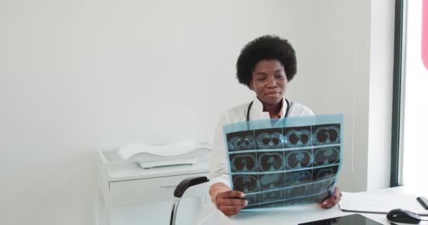 医生检查一个患肺病病人的X光检查。非洲裔美国女医生检查门诊部隆氏X射线检查。穿着白衣的非洲裔美国女医生在医务室很有吸引力 — 图库视频影像