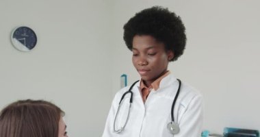 Endokrinolojist, tiroid bezini inceleyen hastalar, iyot yetersizliği semptomu olan kadın doktor, tiroid tiroid hastasının boynuna dokunuyor. Afro-Amerikalı bir doktorda resepsiyondaki genç kız.