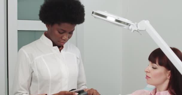 Dermatólogo examina una piel. Médico profesional El dermatólogo investiga una marca de nacimiento en el teléfono conectado a la herramienta especial de la dermatoscopia, antes del procedimiento del retiro del laser de una marca de nacimiento. — Vídeos de Stock