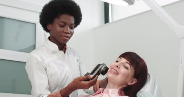 Medicul este un dermatolog afro-american care examinează pielea. Medicul profesionist Dermatologul de cercetare un semn de naștere pe telefon conectat la instrumentul special de dermoscopie. Examinarea feței — Videoclip de stoc