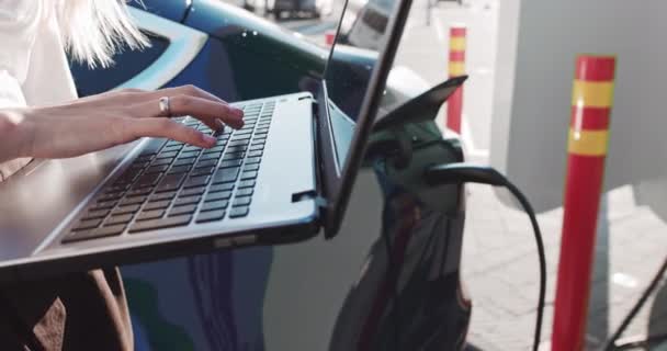 Close-up Shot: Pessoa digitando no teclado do computador. Trabalhando, escrevendo e-mails, usando a Internet. As mãos femininas pressionam botões do portátil, no fundo que carrega o carro elétrico. Trabalhar à distância. Negócios — Vídeo de Stock
