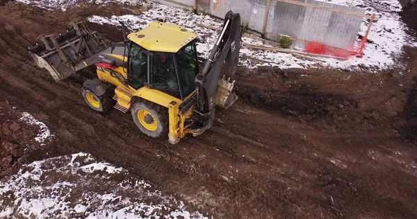 Трактор на будівництві будинку. Розстріл безпілотника, перекриття трактора, що їде по ґрунтовій дорозі. Працівник перевіряє якість бетону фундаменту. Будівництво промислового об'єкта — стокове фото