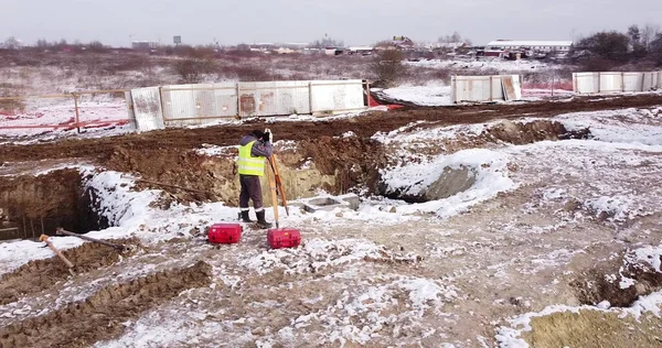 Trabajador de la construcción utilizando el instrumento óptico de levantamiento de teodolitos para medir ángulos en planos horizontales y verticales en el sitio de construcción. Ingeniero Arquitecto comprueba la calidad de la construcción — Foto de Stock