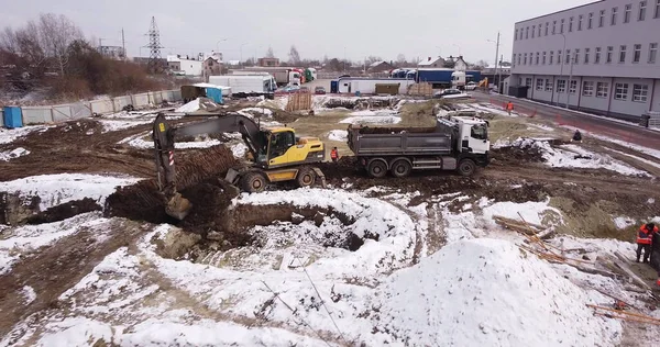 Aerial top view: yellow excavator pouring soil into tipper. Preparing place to construction residential house. top down view of an excavator loading crushed stone into a dump truck in a crushed stone