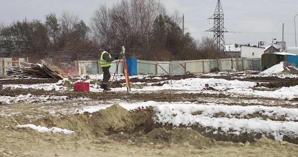 Munkás profi földmérnök Az építkezésen a kezében két piros bőrönd. Teodolit geodéziai optikai műszert alkalmazó munkavállaló a szögek mérésére különböző síkokban — Stock Fotó