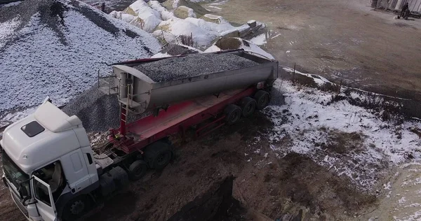 En stor, moderne lastebil heller i grus eller skyter på bakken. Levering av byggevarer til bygging. Droneskyting, overflyging av lossemateriale for lastebiler stockfoto