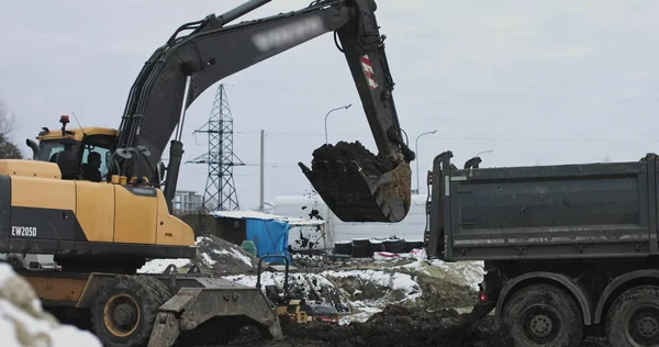 Excavadora en acción en el sitio de construcción. disparo: cubo tractor está llenando un cuerpo de camión. Una excavadora y un camión están cargando tierra. Preparación para la construcción de una instalación industrial — Foto de Stock