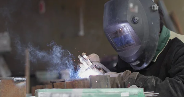 Close-up blacksmith welder in protective mask works with metal steel and iron using a welding machine, bright sparks and flashes in extreme slow motion — Stock Photo, Image