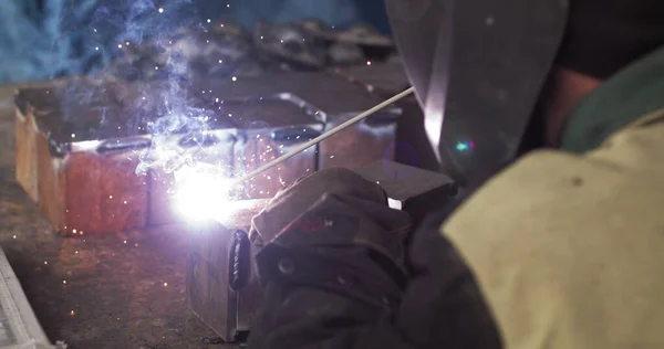 El soldador de herrero de primer plano en máscara protectora trabaja con metal usando una máquina de soldadura, chispas brillantes y destellos en cámara súper lenta —  Fotos de Stock