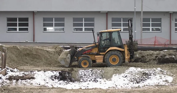 La excavadora trabaja en un sitio de construcción con arena, vista lateral. Nuevo Big Tractor, una excavadora sobre ruedas en un camino arenoso en una obra de construcción allana el sitio para la construcción de bienes raíces — Foto de Stock