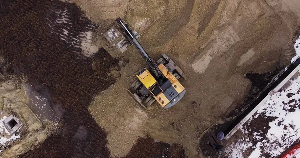 Uma escavadeira industrial em uma seção de estrada aberta carrega rocha e terra em um caminhão de descarga muito grande, carregado com minério. O balde da escavadeira goteja e carrega o minério. Panorama de obras de construção. — Fotografia de Stock